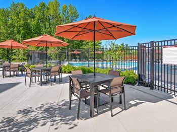 a patio with tables and umbrellas near a swimming pool